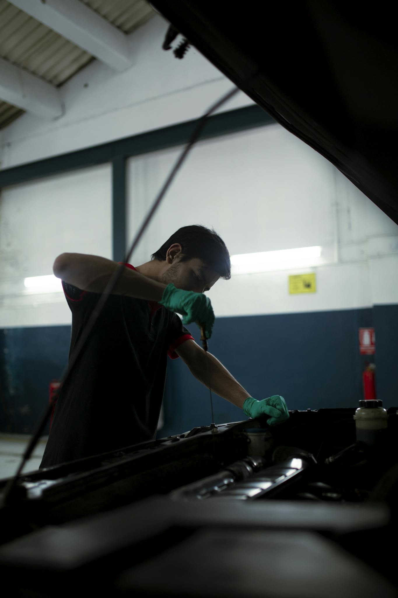 Mechanic checks engine oil in a car inside an auto garage, highlighting routine maintenance.